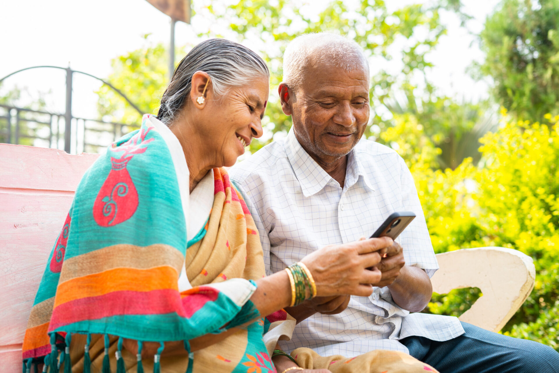 MN Health Senior couple using mobile phone while sitting on park - concept of social media, technology lifestyles and relaxation